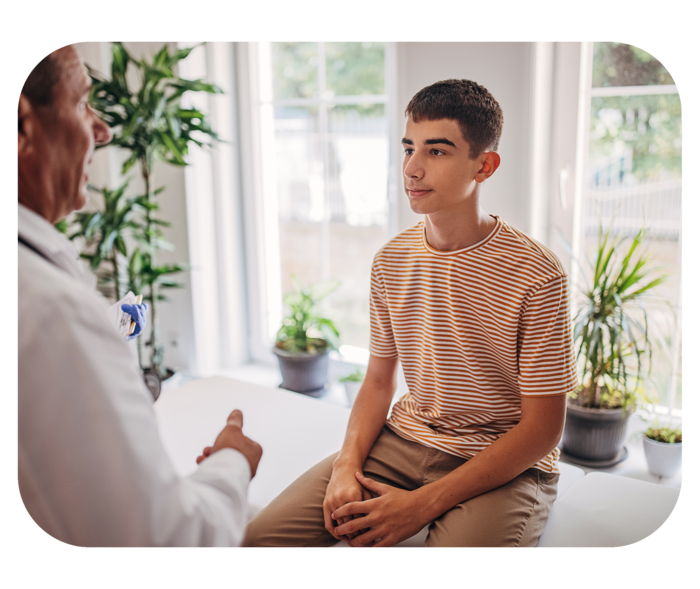 Transition: Der Wechsel in die Erwachsenenmedizin Jugendlicher sitzt auf einer Behandlungsliege. Ihm gegenüber steht ein Mann mit weißem Kittel.