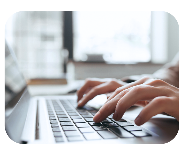 Hände tippen auf der Tastatur eines aufgeklappten Laptops.