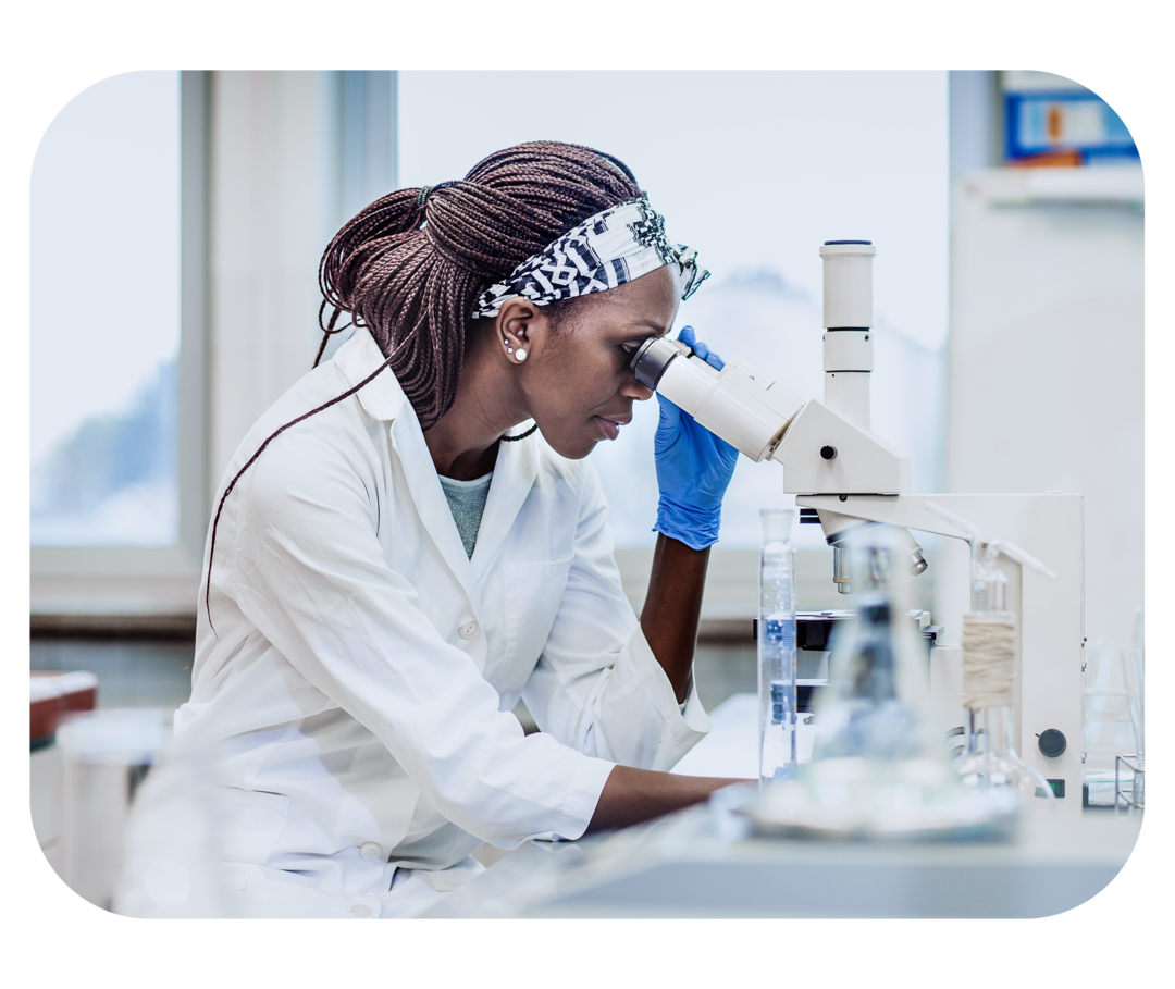 Eine Frau in weißem Kittel schaut durch ein Mikroskop. 