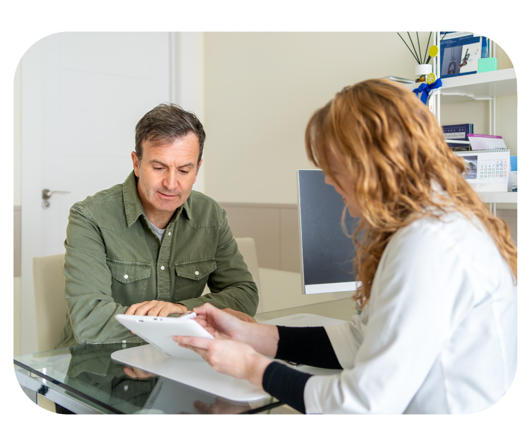 Diagnose chronischer Nierenerkrankungen Eine Frau mit weißem Kittel sitzt an einem Tisch und unterhält sich mit einem Mann, der ihr gegenübersitzt.
