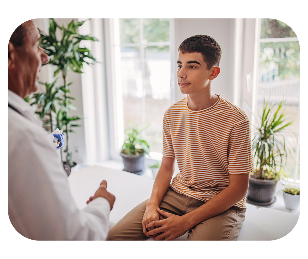 Transition: Der Wechsel in die Erwachsenenmedizin Jugendlicher sitzt auf einer Behandlungsliege. Ihm gegenüber steht ein Mann mit weißem Kittel.
