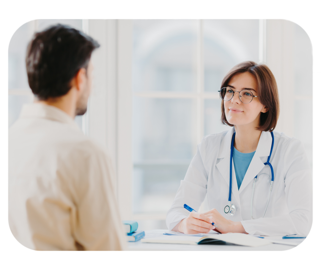 Mann sitzt Frau mit weißem Kittel gegenüber. 