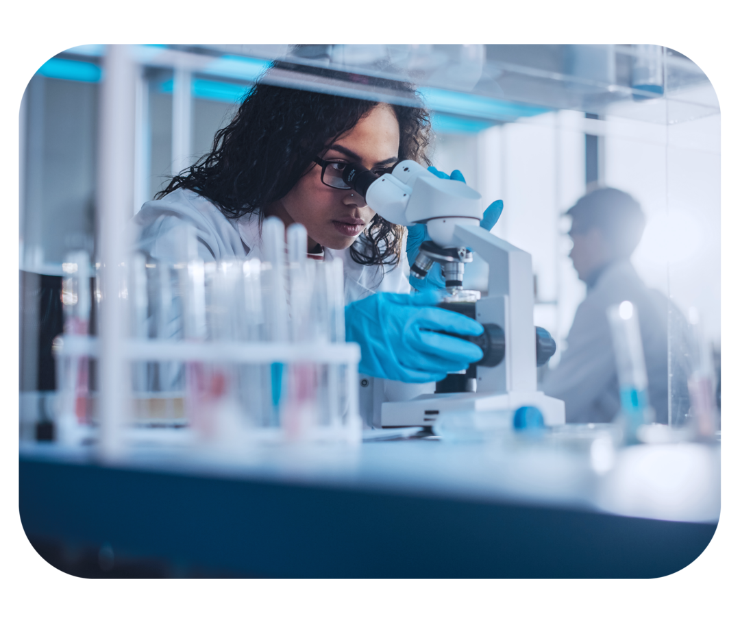 Eine Frau steht in einem Labor und schaut durch ein Mikroskop.