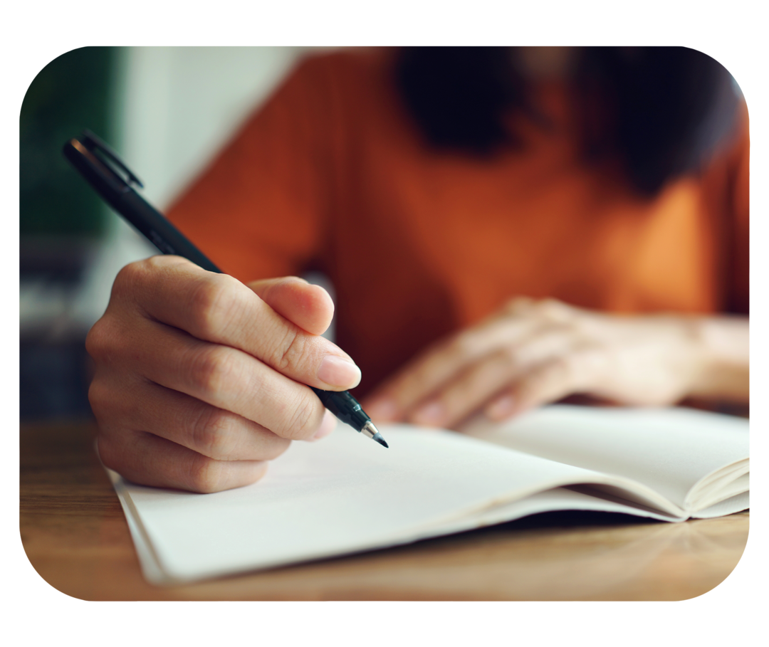 Hand einer Person, die einen Stift über einem Notizbuch hält.