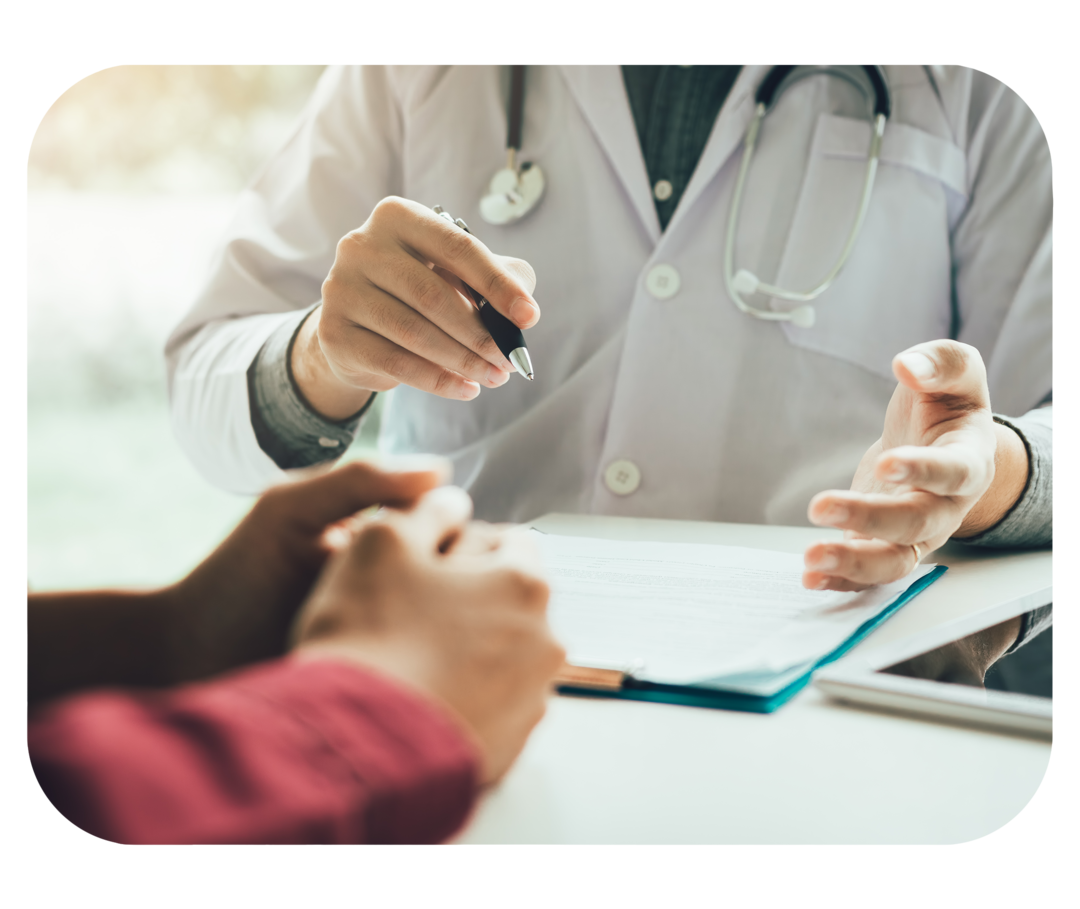 Person mit weißem Kittel sitzt an einem Tisch. Gegenüber sitzt.