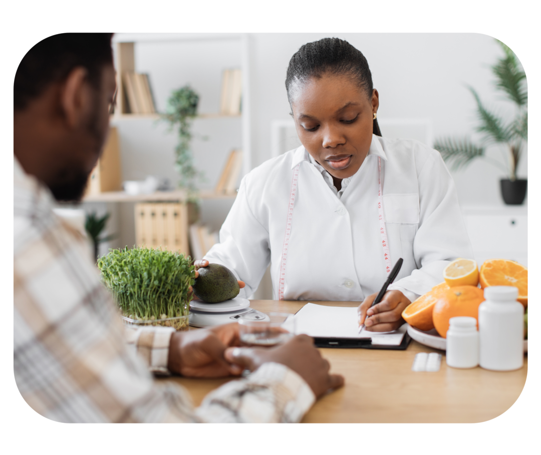 Eine Ärztin sitzt an einem Tisch macht sich Notizen zu einem Mann, der ihm gegenübersitzt. 