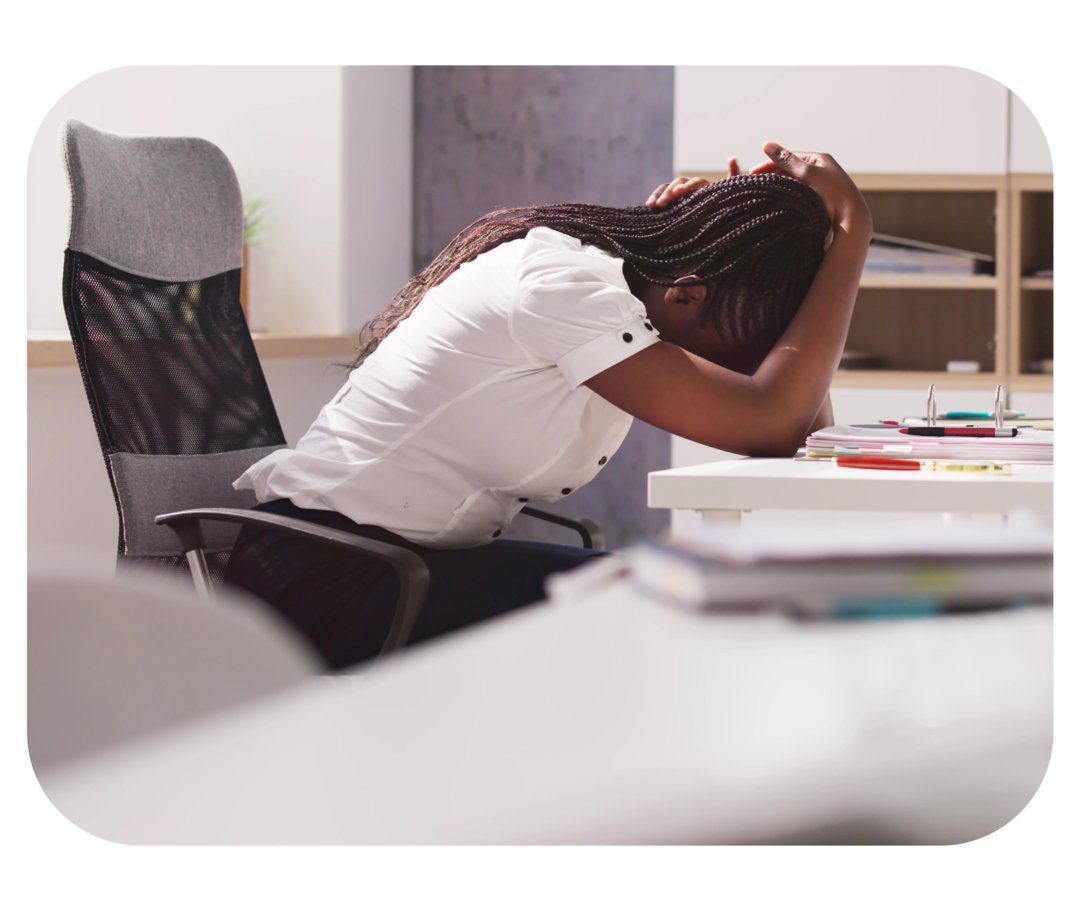 Frau sitzt am Schreibtisch und hat den Kopf in die Hände gelegt.