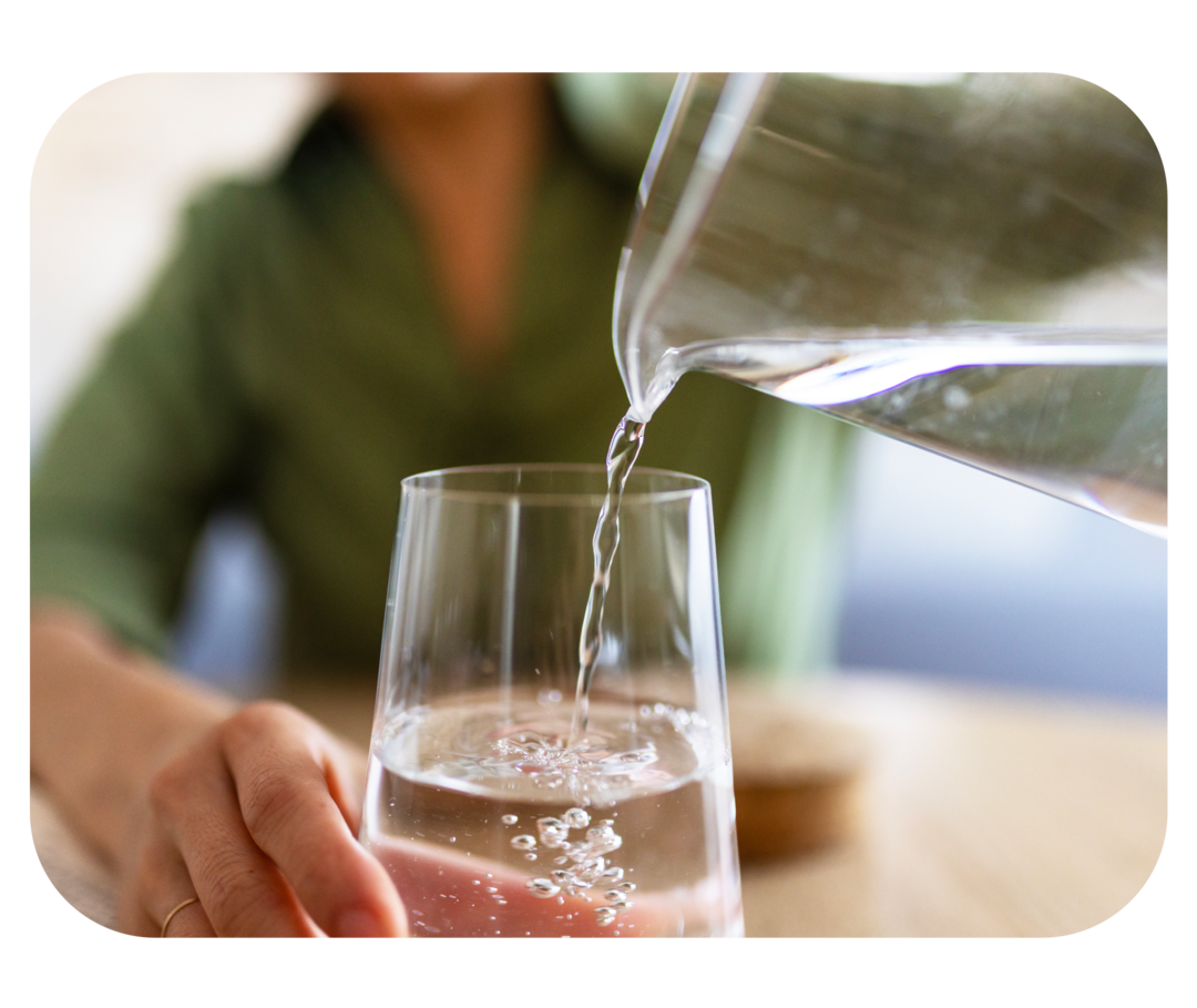  Eine Person gießt Wasser aus einem Krug in ein Glas.