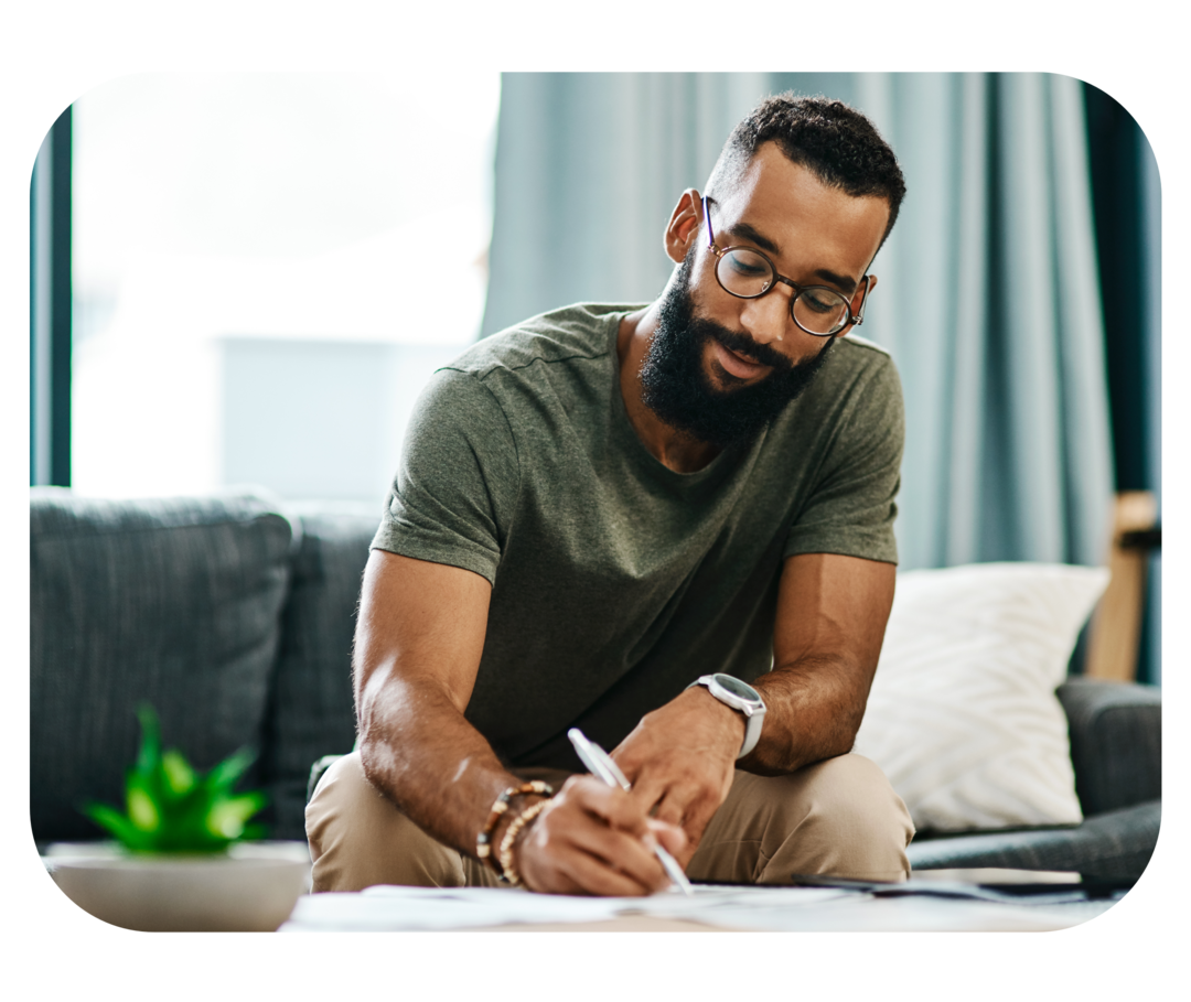 Ein Mann sitzt auf einem Sofa und geht Papiere durch, die vor ihm auf einem Tisch liegen.