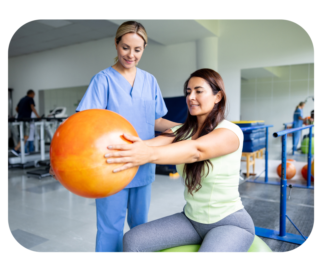 Eine Frau sitzt auf einem Gymnastikball und hält einen Ball. Dahinter steht eine weitere Frau.